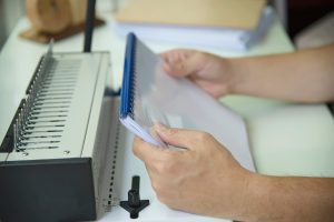 Man making report using comb binding machine - people working with stationary tools concept